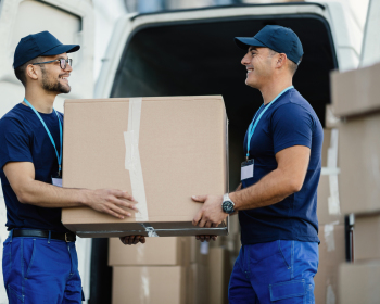Happy delivery men unloading cardboard box from a mini van.